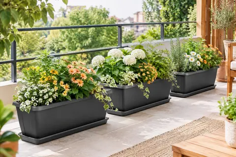 Trois jardinières rectangulaires anthracite avec soucoupes, garnies de fleurs et de feuillages sur un balcon