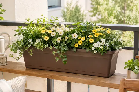 Jardinière rectangulaire marron en plastique, garnie de fleurs et de feuillages sur un balcon aménagé.